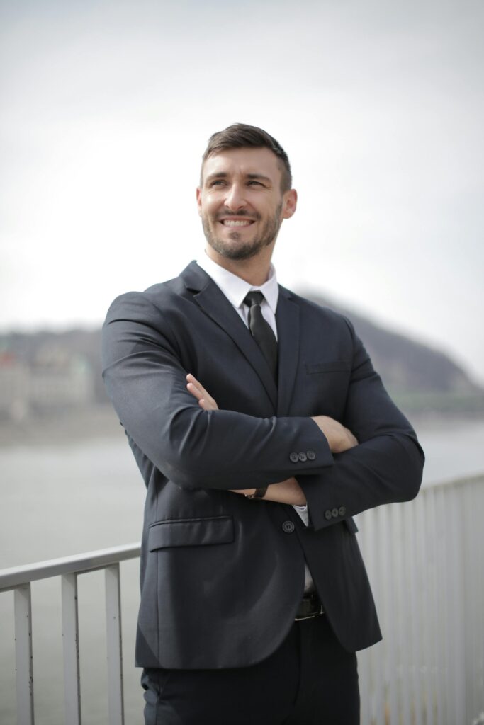 Smiling businessman in a suit standing confidently outdoors by the river.