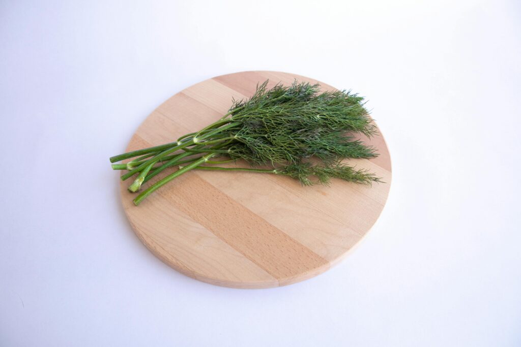Top view of fresh dill on a wooden round cutting board, ideal for culinary themes.