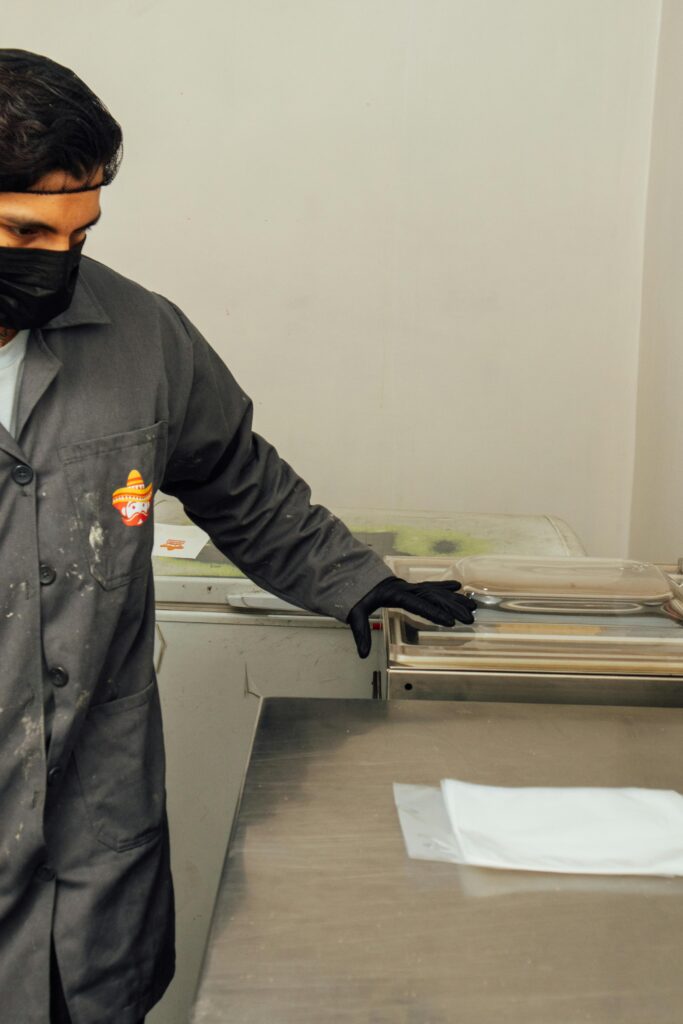 Male industrial worker wearing mask and gloves operating a machine in a factory setting.